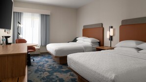 Ein Hotelzimmer mit zwei Betten, einem Schreibtisch, einem Stuhl, einem Fernseher und einem Fenster mit Vorhängen.