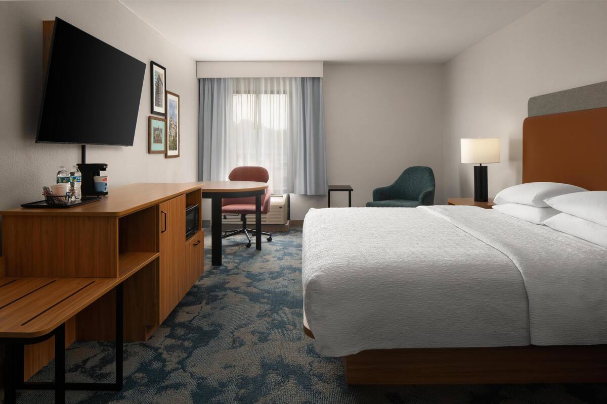 A hotel room with a bed, desk, chair, TV, and a window with curtains.