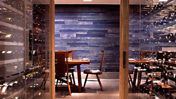 A wine cellar with glass walls, a wooden table, and chairs.