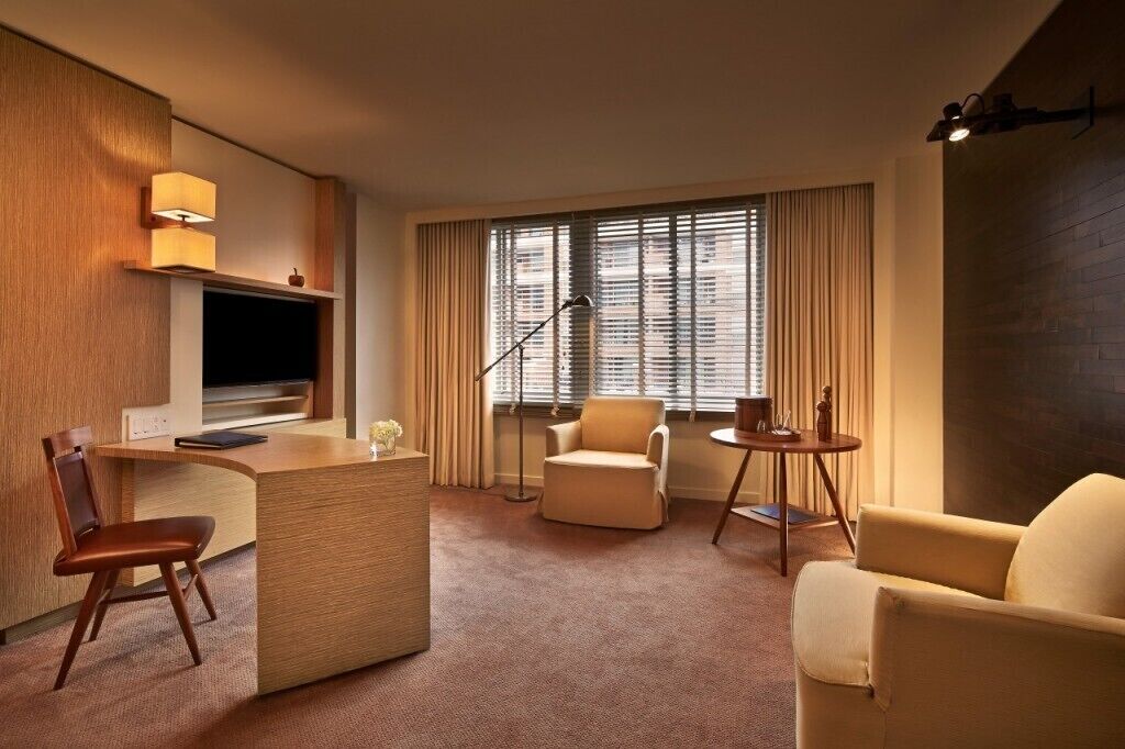 A hotel room with a wooden desk, a flat-screen TV, a sofa, a chair, and a small table with a lamp.