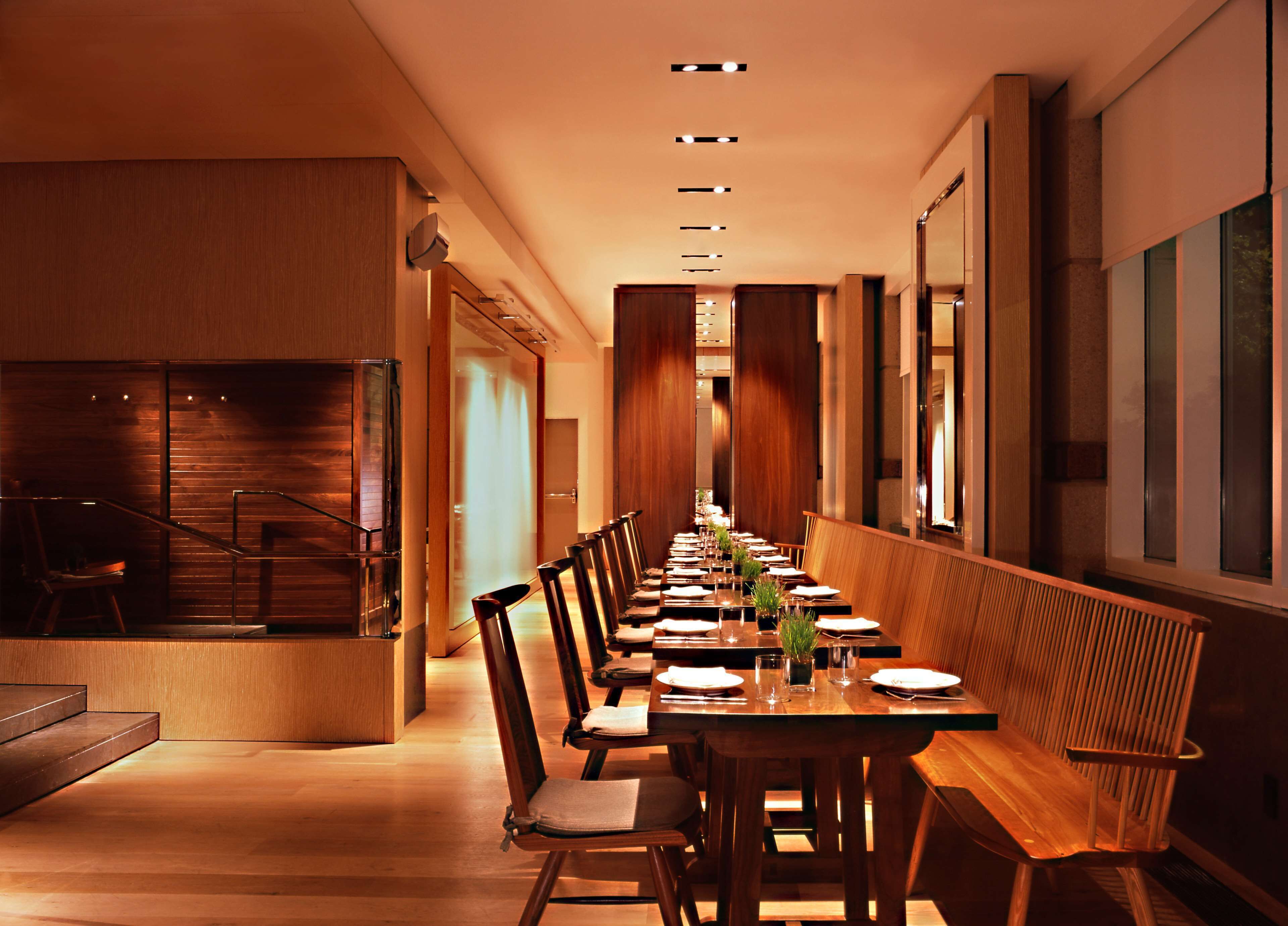 A long dining table with chairs, a staircase, and a wooden wall.