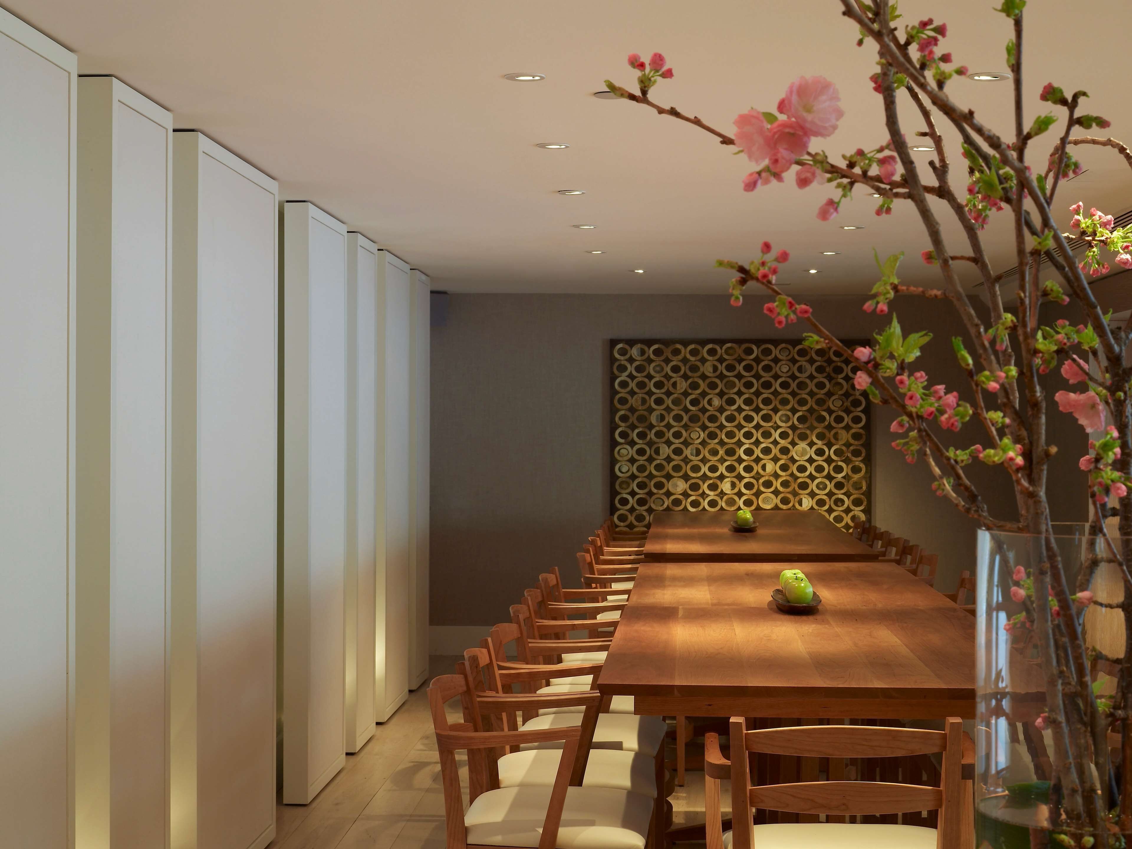 A dining area with a long wooden table, several chairs, a vase with flowers, and a decorative wall panel.