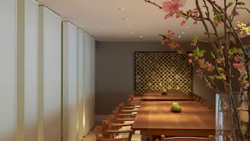A dining area with a long wooden table, several chairs, a vase with flowers, and a decorative wall panel.