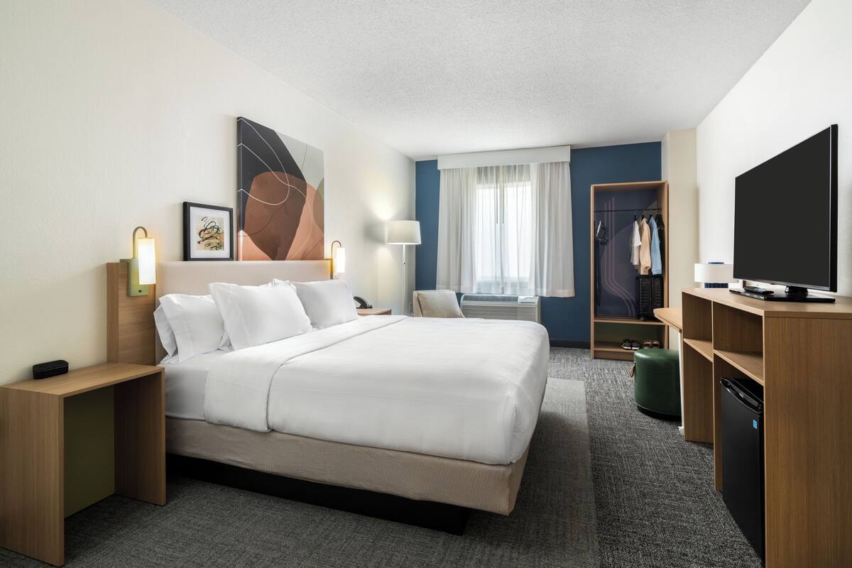 Une chambre d’hôtel avec un grand lit, un bureau avec une télévision, une armoire et une fenêtre avec des rideaux.