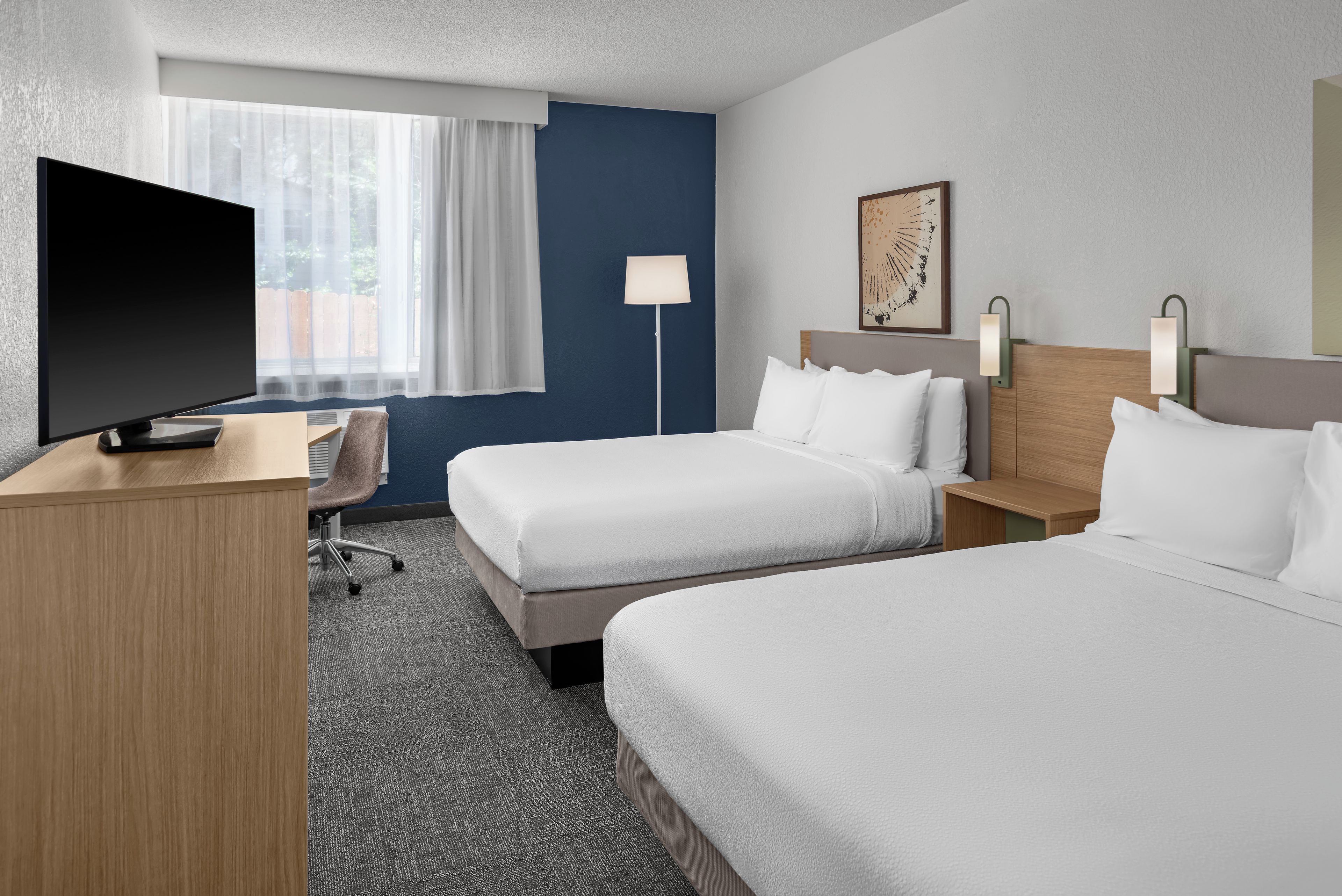 Habitación de hotel con dos camas, un escritorio, un televisor y una ventana con cortinas.