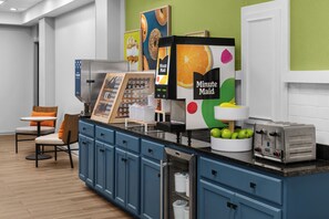 A self-service breakfast area with a yogurt machine, a toaster, and a fruit bowl. - Spark by Hilton Kansas City Plaza Streetcar (Kansas City)