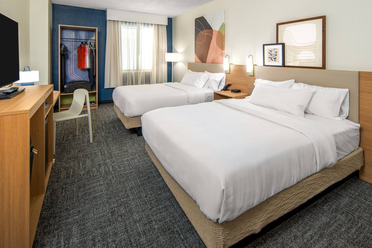 Une chambre d’hôtel avec deux lits, un bureau avec une chaise, un porte-manteau et un téléviseur.