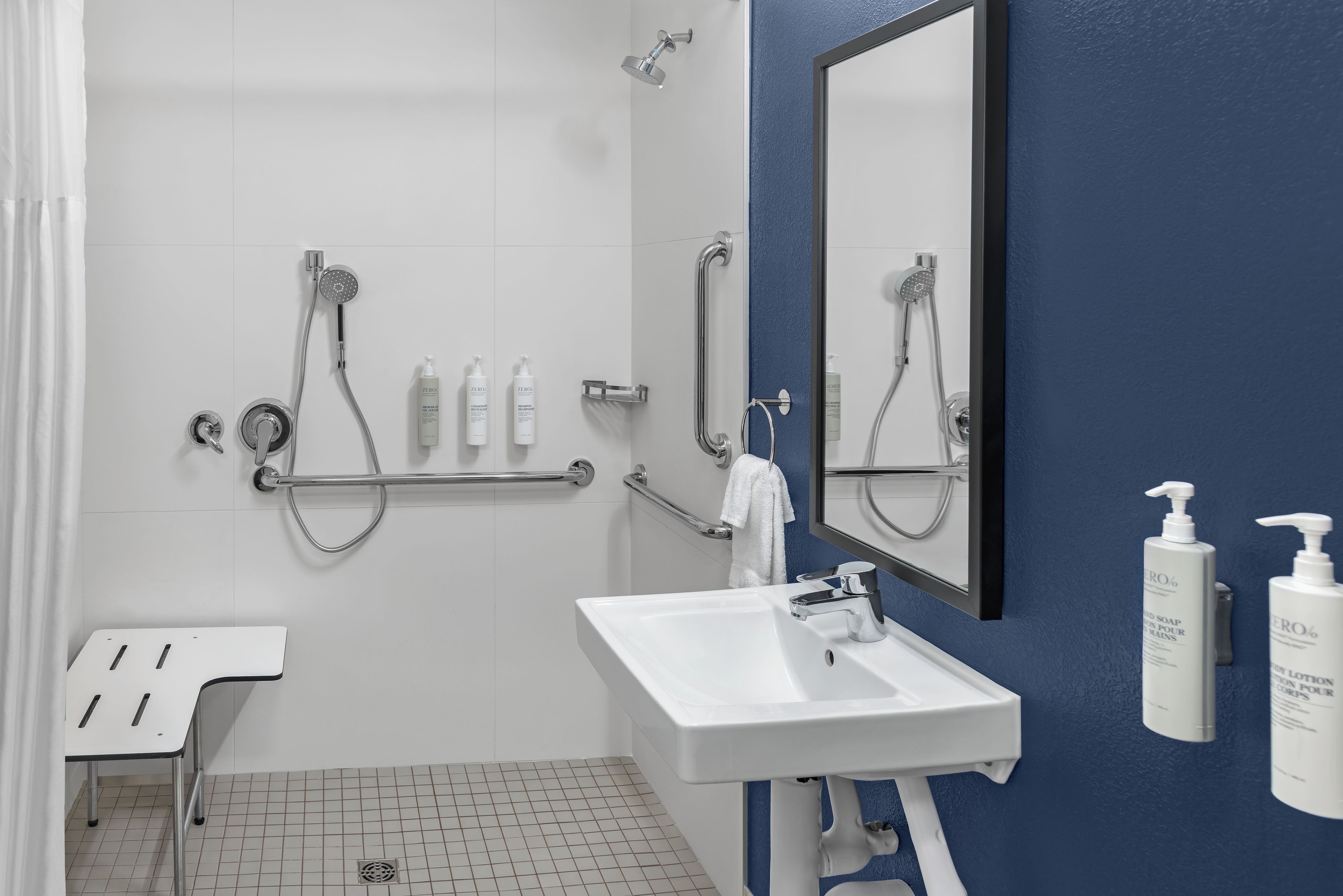 Un baño moderno con un lavamanos blanco, un espejo y una ducha con barras de apoyo.