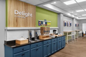 A breakfast bar with a wooden wall, a green accent wall, and a sign that reads 'Delight in the day'. - Spark by Hilton Kansas City Plaza Streetcar (Kansas City)