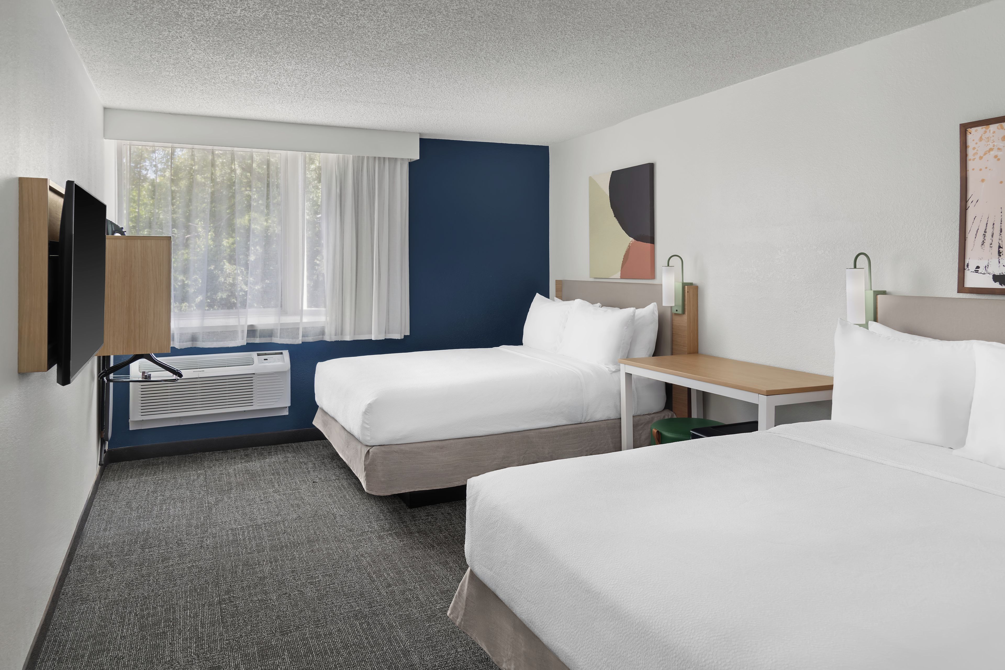 Habitación de hotel con dos camas, televisión, escritorio, lámpara y ventana con cortinas.