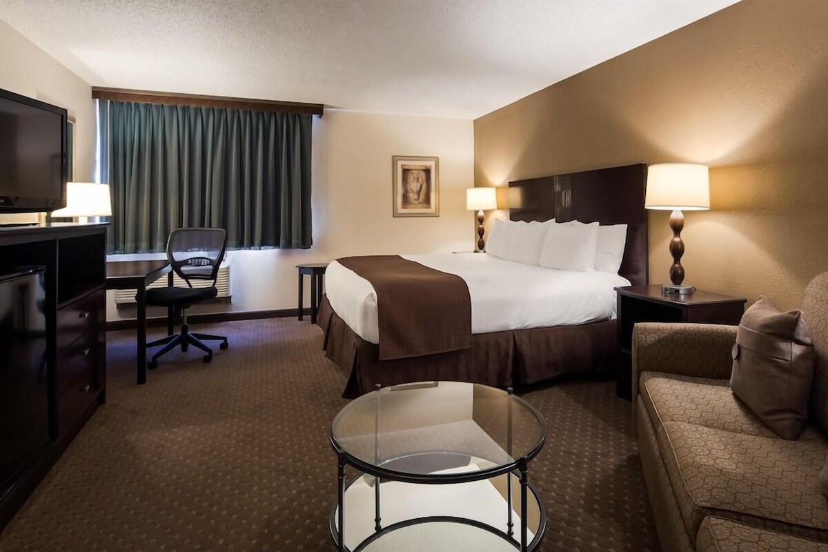 Ein Hotelzimmer mit einem Bett, einem Schreibtisch mit Fernseher, einem Sessel, einem Glastisch und einem Sofa.