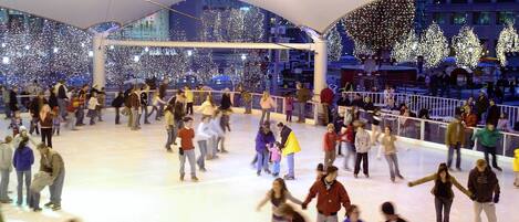 An indoor ice skating rink with a crowd of people, some on the ice and others watching.