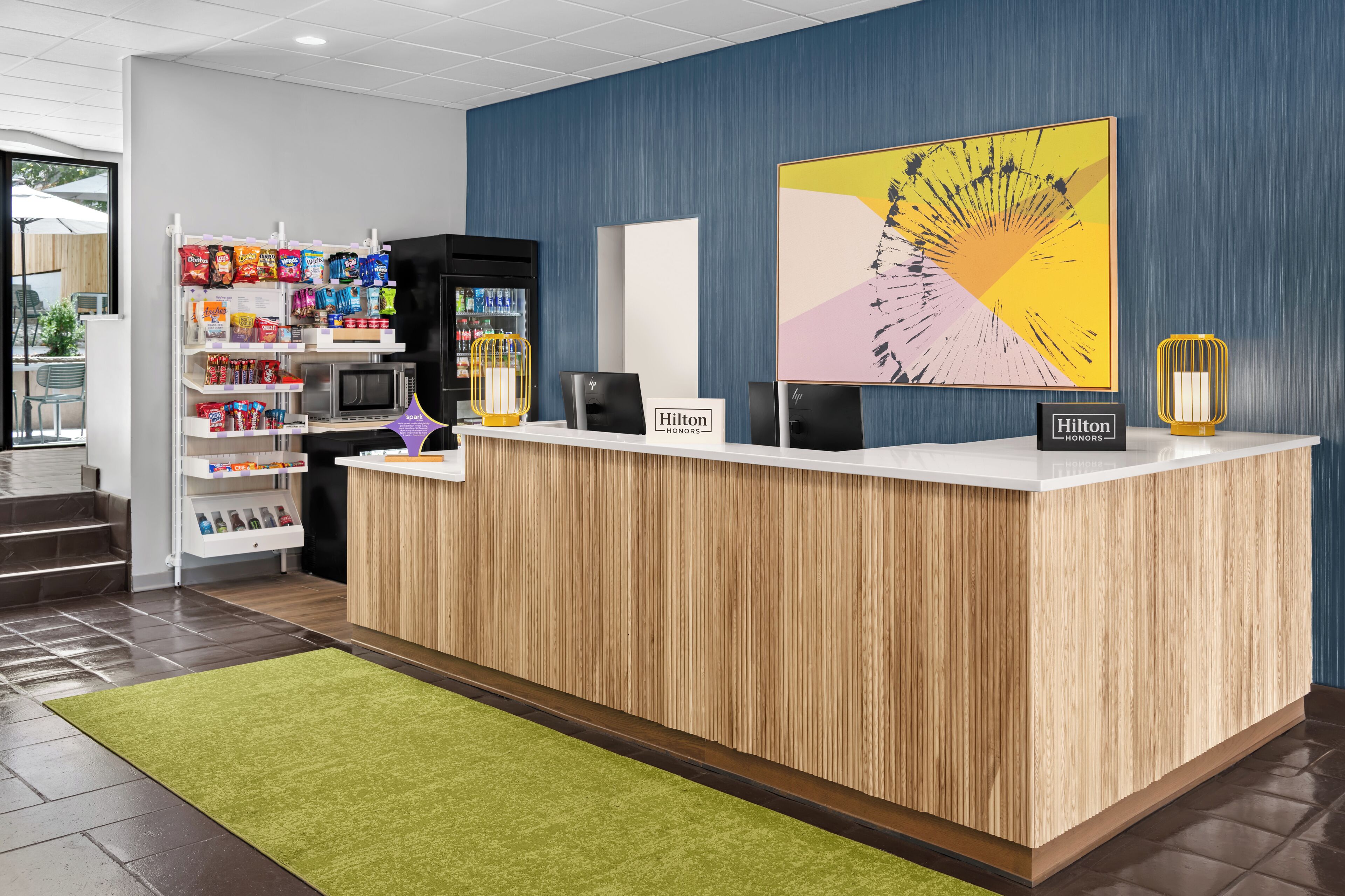 A hotel reception desk with a wood panel design, a vending machine, and a large abstract painting.