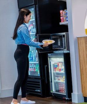 A person holding a plate with food near a black appliance, possibly a microwave, with a freezer below it.