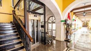 Un hall d’hôtel avec un escalier, un ascenseur et une statue.