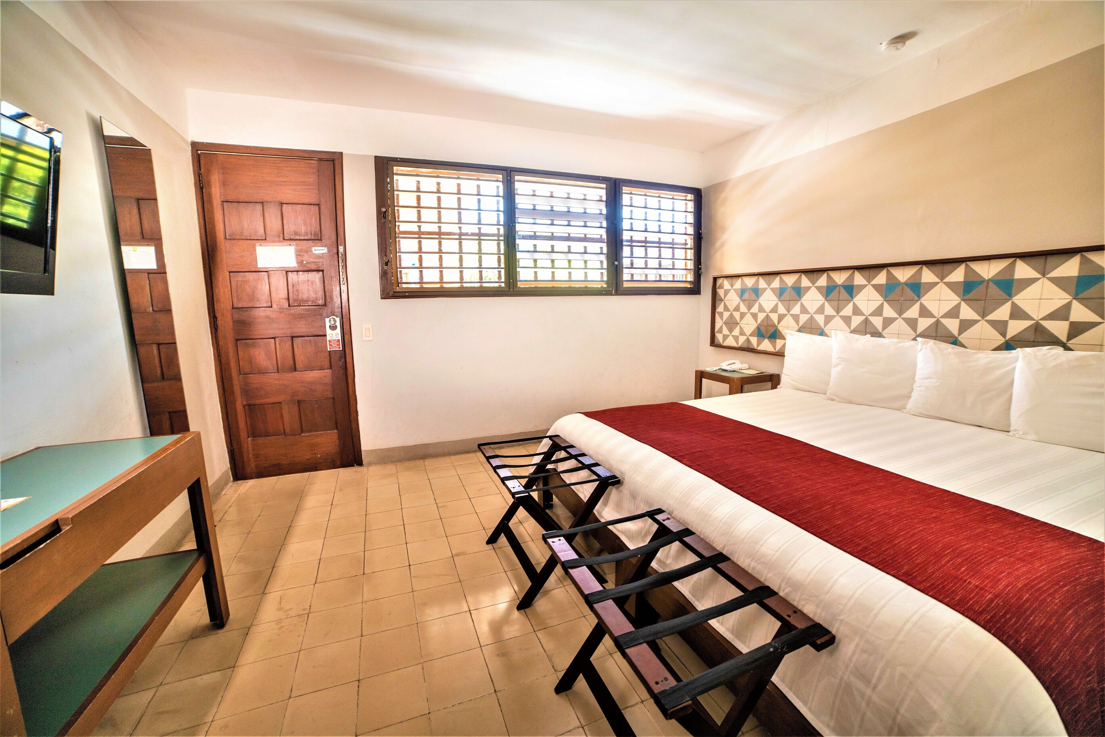 A hotel room with a bed, a desk, a chair, a window, and a door.