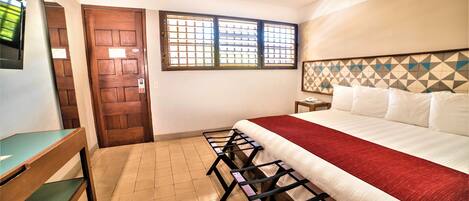 A hotel room with a bed, a desk, a chair, a window, and a door.