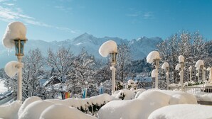 Een besneeuwde buitenruimte met lantaarns en bomen, met daarbuiten een bergpanorama.
