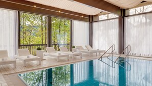Zona de piscina con sillas reclinables blancas y vista despejada a árboles a través de amplios ventanales.
