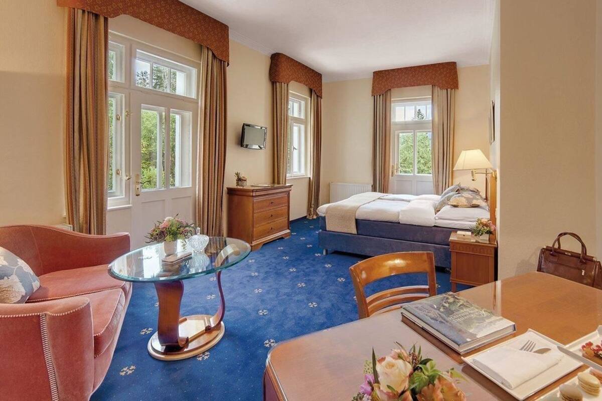 Hotelkamer met een bed, een glazen salontafel, een bank, een eettafel en een televisie.