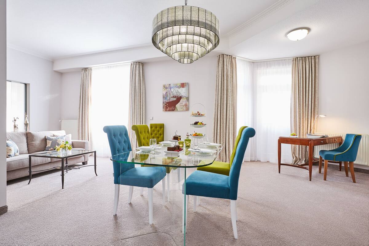 Een moderne eetruimte met een glazen tafel, blauwe stoelen en een kroonluchter.