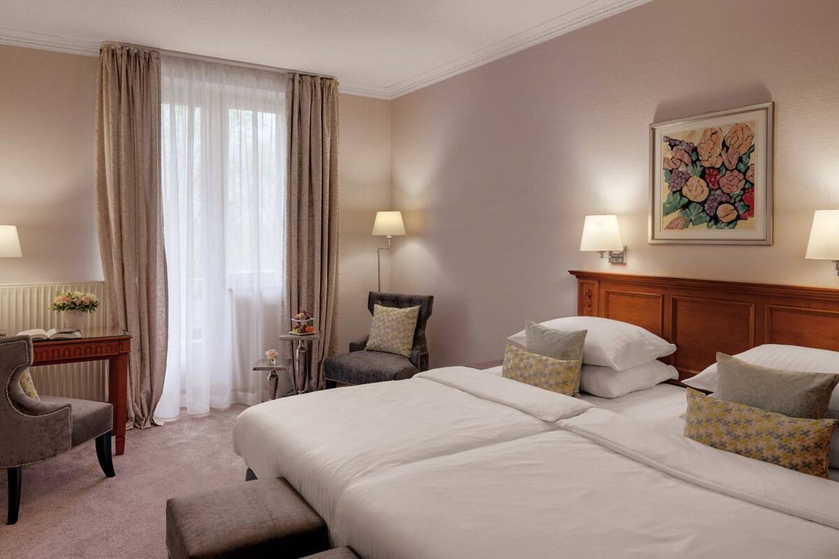Hotelkamer met een groot bed, een bureau met lamp, een stoel en een klein tafeltje met lamp.