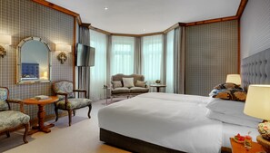 Una habitación de hotel con una cama grande, un sofá, una silla, una mesita y un televisor.