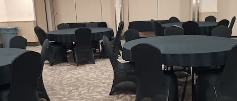 A conference room with multiple tables and chairs, carpeted flooring, and ceiling lights.