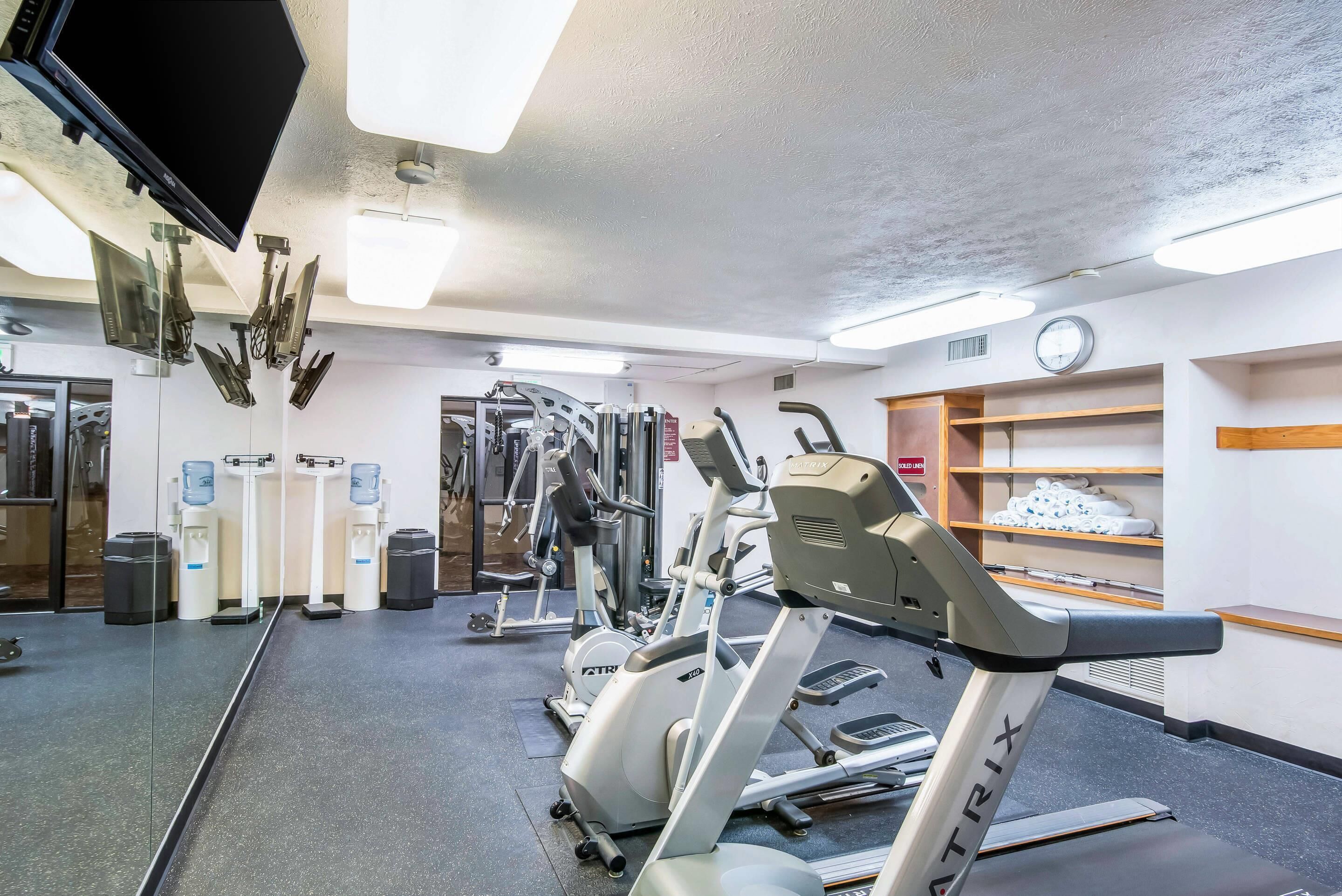 A gym with exercise equipment, a water dispenser, a clock, and a shoe shelf.