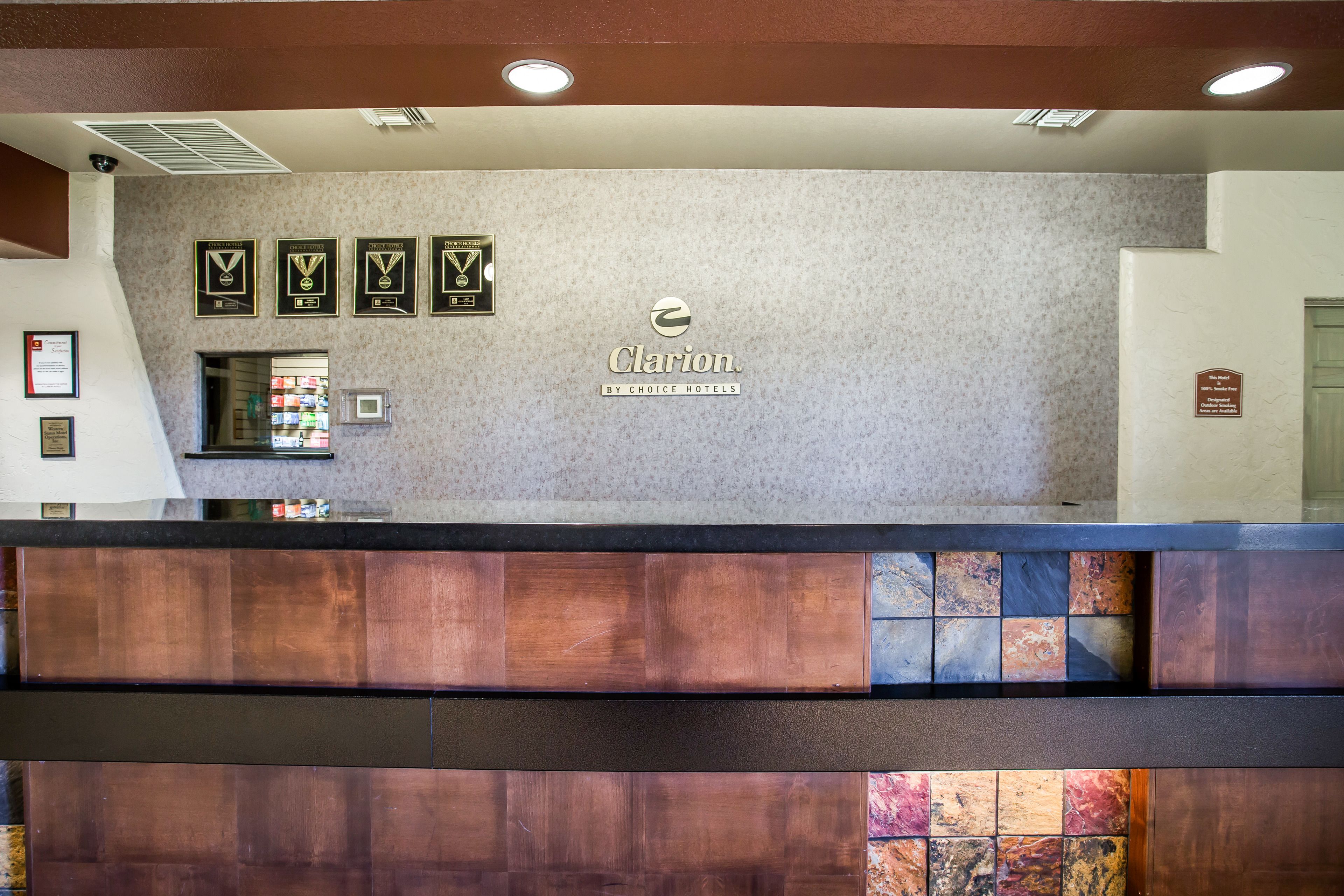 A reception desk with a logo for Clarion by Choice Hotels, framed awards on the wall, and a view of the lobby area.