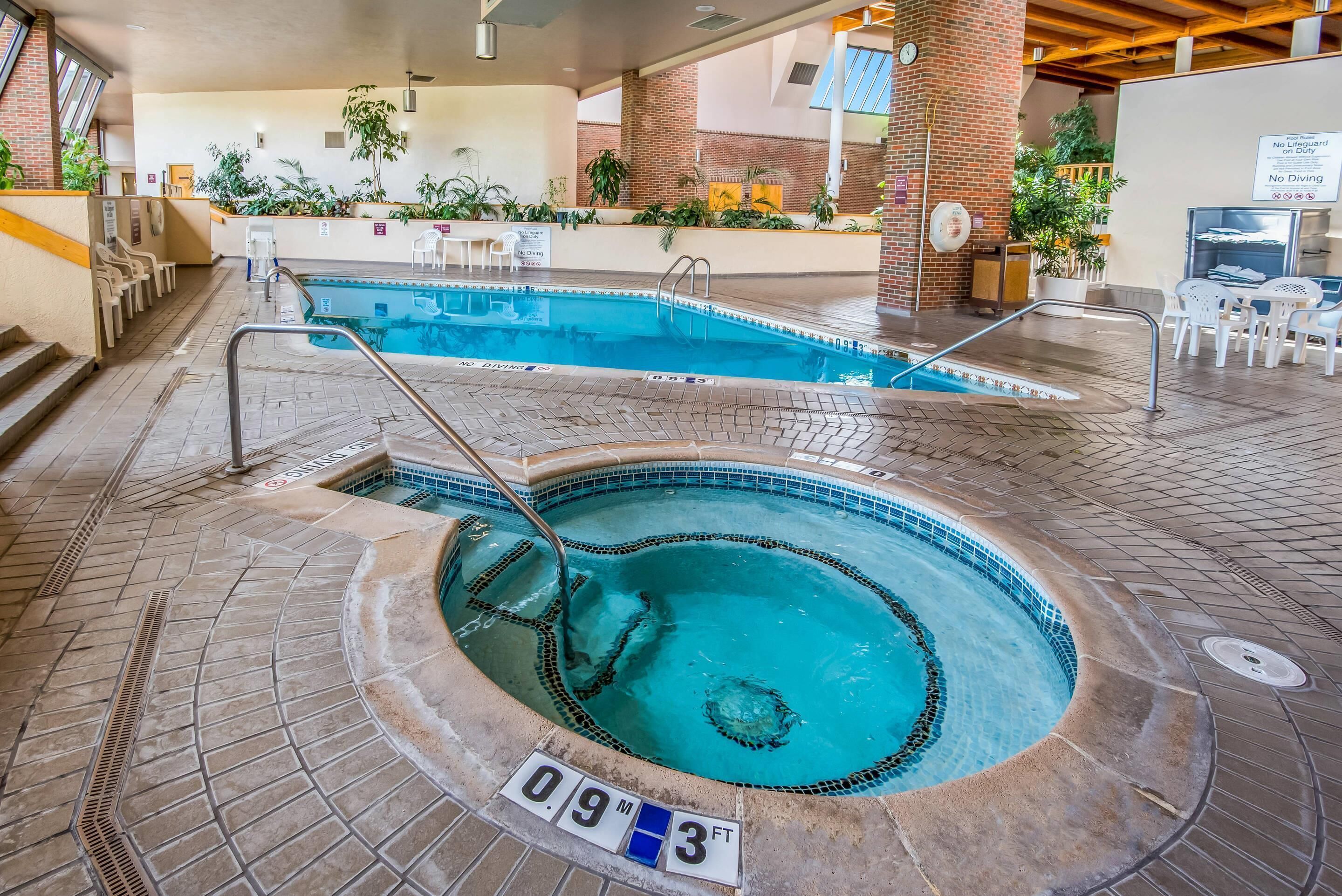 An indoor pool with a hot tub, a lifeguard sign, and a sign indicating no diving.
