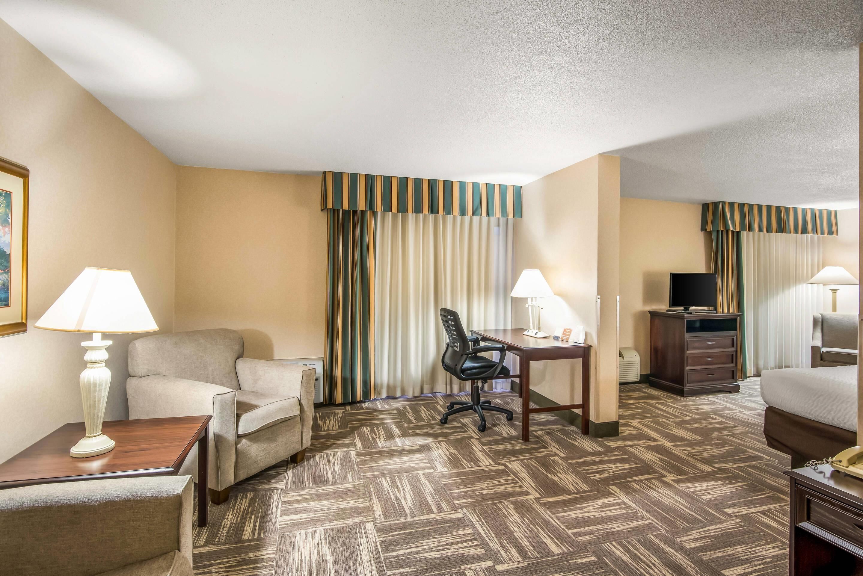 A hotel room with a sofa, desk, chair, lamps, TV, and a bed.