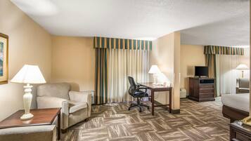 A hotel room with a sofa, desk, chair, lamps, TV, and a bed.
