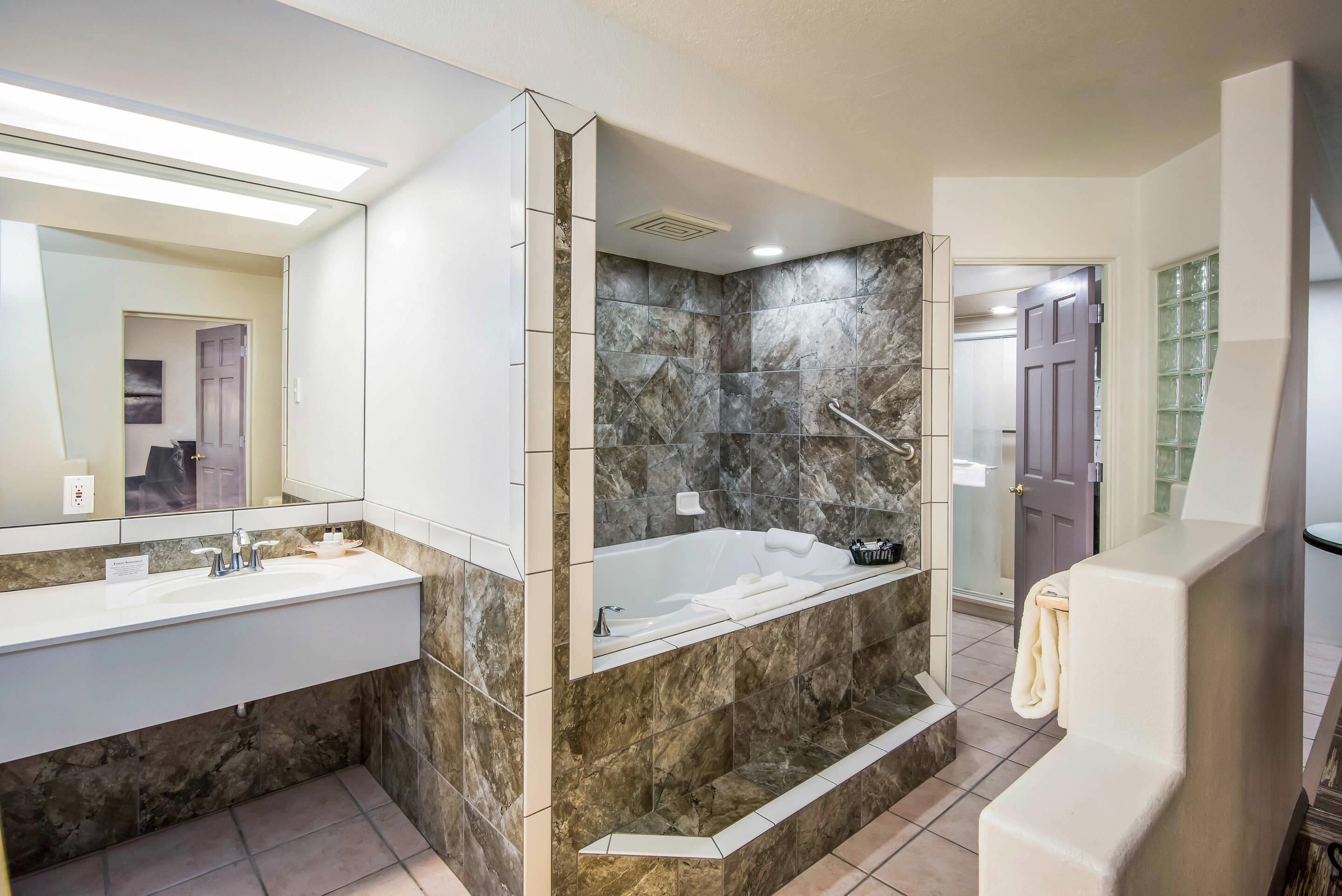 A modern bathroom with a large mirror, a bathtub, a shower, and a vanity with a sink.