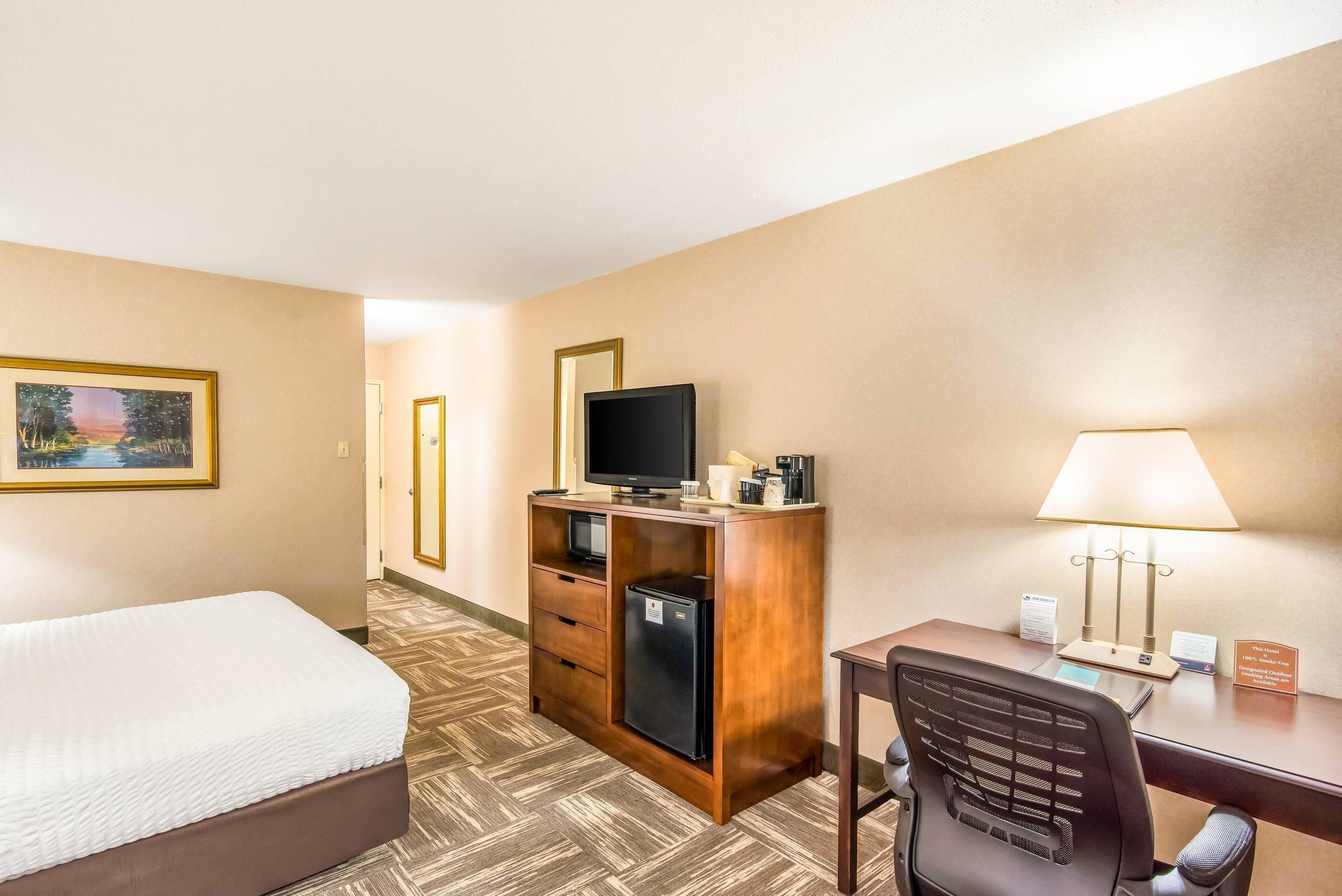 Une chambre d’hôtel équipée d’un lit, d’un bureau avec un ordinateur, d’un réfrigérateur, d’une télévision et d’une lampe.