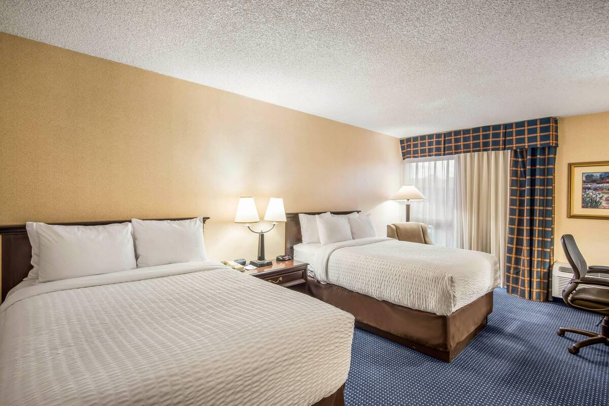 A hotel room with two beds, a desk, a chair, and a window with curtains.