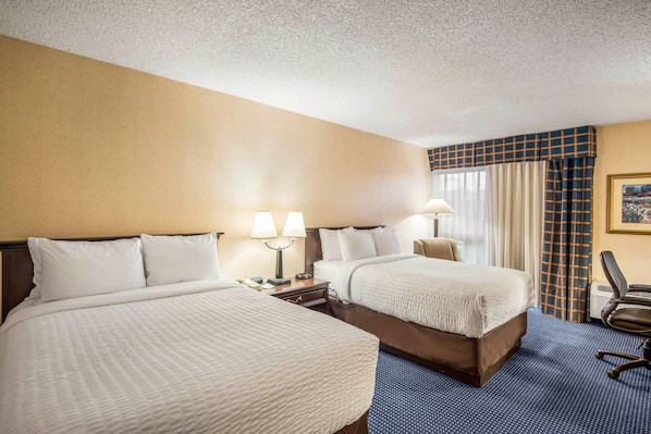 A hotel room with two beds, a desk, a chair, and a window with curtains.