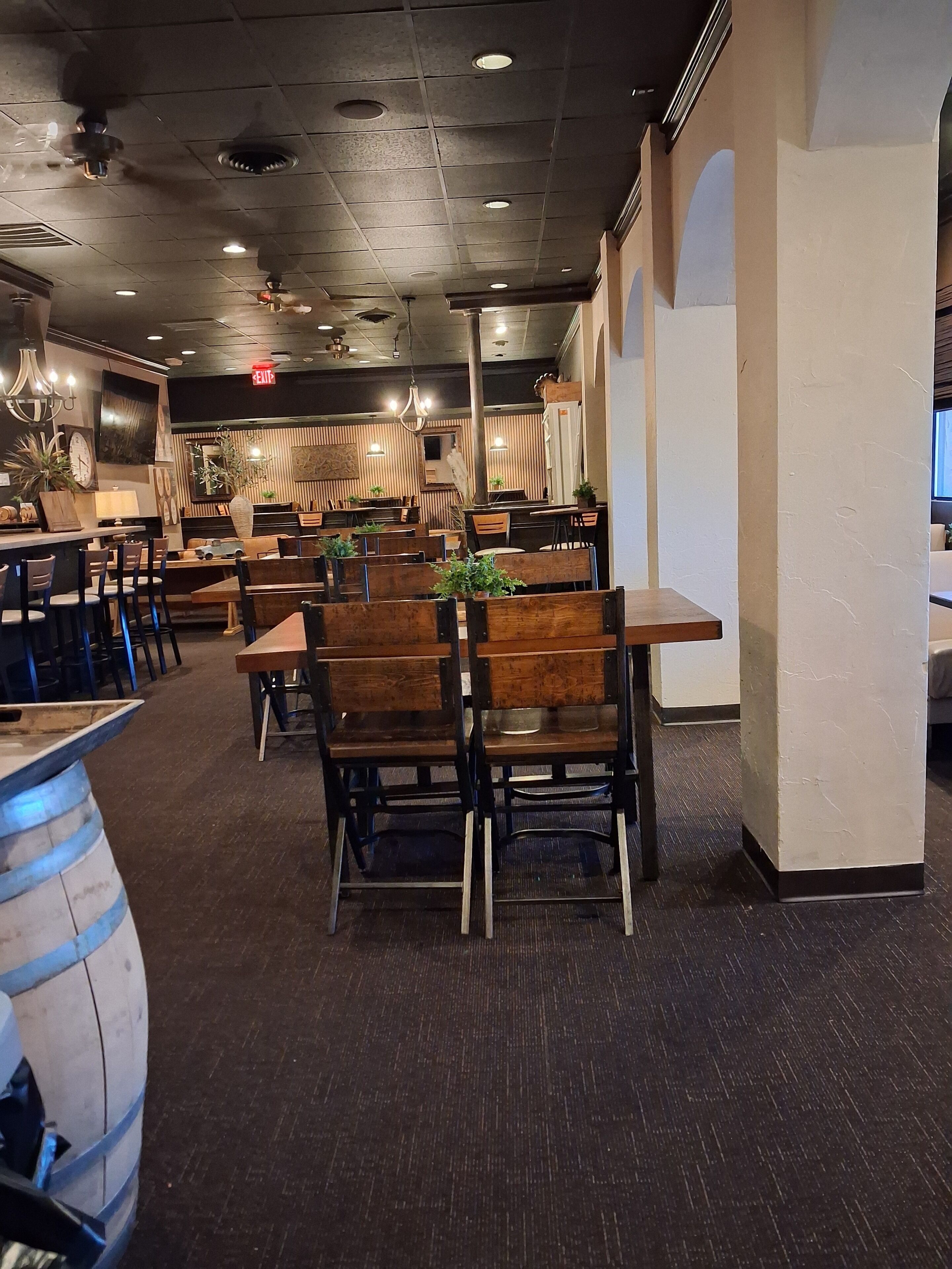 A restaurant interior with wooden tables and chairs, ceiling fans, recessed lighting, and a patterned wall.