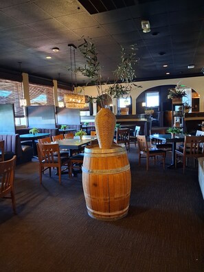 A restaurant interior with wooden tables and chairs, hanging plants, and a large barrel centerpiece. - Clarion Inn Grand Junction (Grand Junction)
