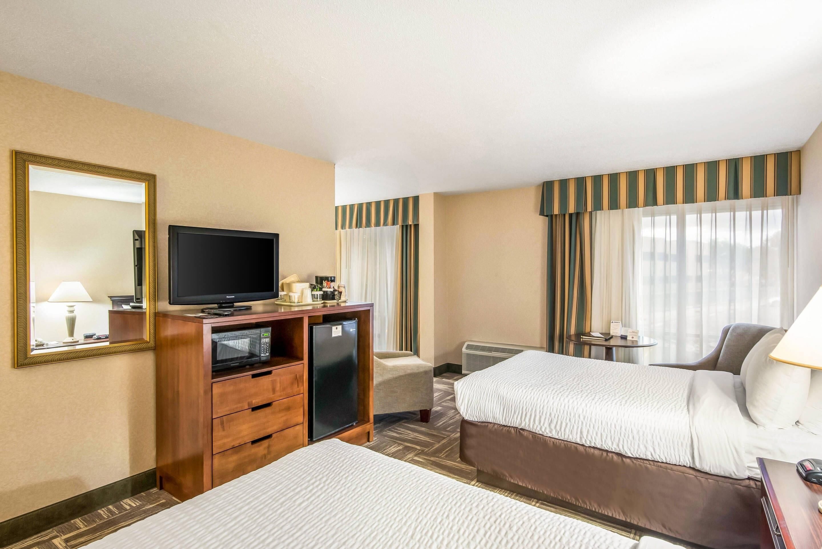 A hotel room with two beds, a TV, a minibar, a desk, and a chair.