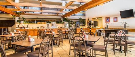 Un restaurante espacioso con techos altos de madera, varias mesas y sillas para comer, una zona de cocina y un televisor de pantalla plana en la pared.