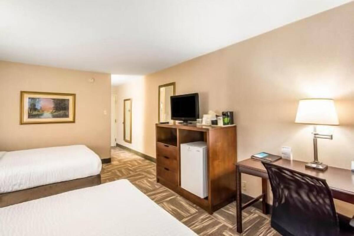 A hotel room with a bed, a desk with a computer, a television, and a lamp.