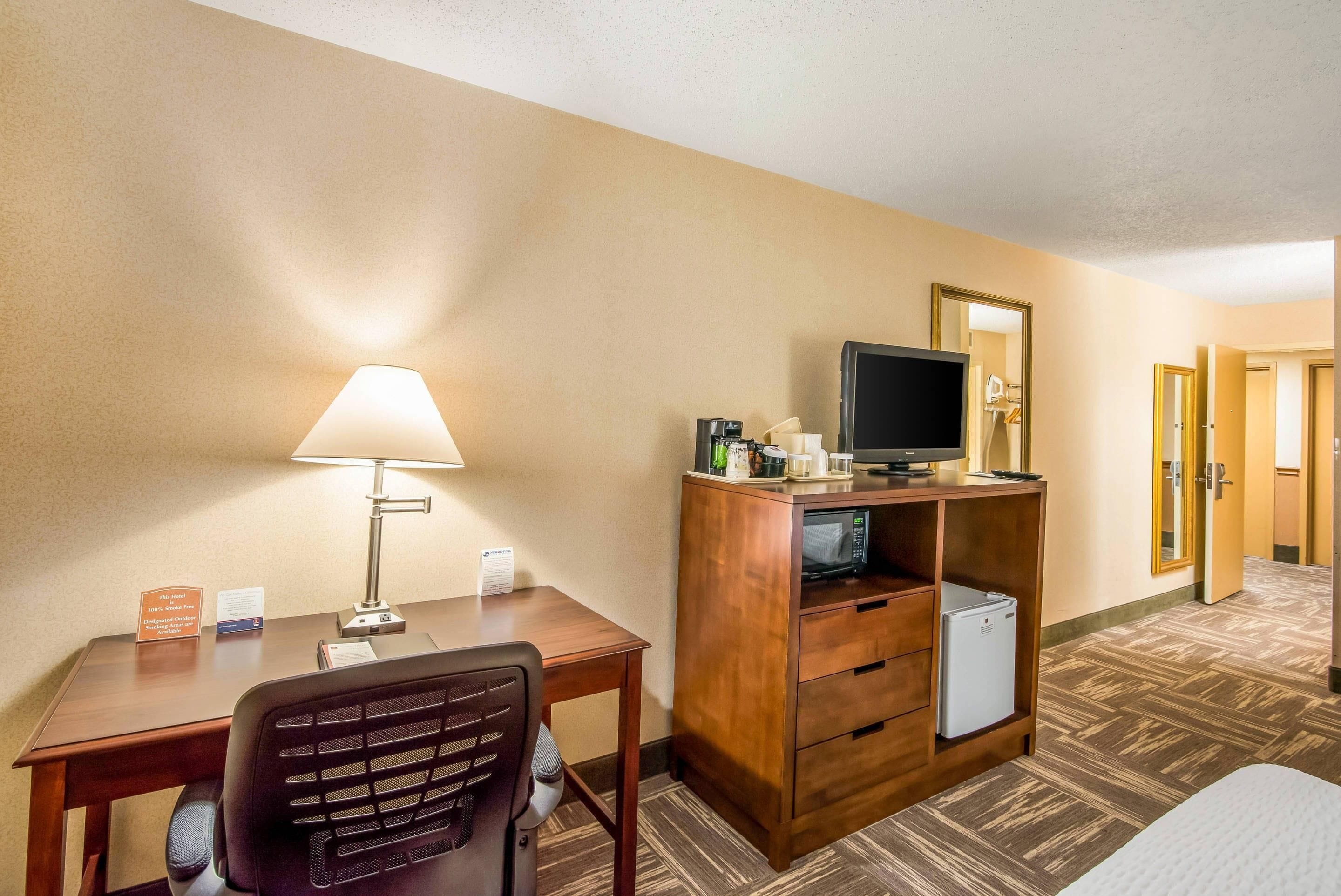 Une chambre d’hôtel équipée d’un bureau, d’une chaise, d’une lampe, d’une télévision, d’un minibar et d’un miroir.