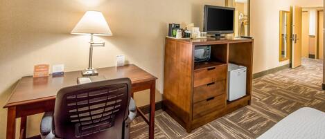 Une chambre d’hôtel équipée d’un bureau, d’une chaise, d’une lampe, d’une télévision, d’un minibar et d’un miroir.