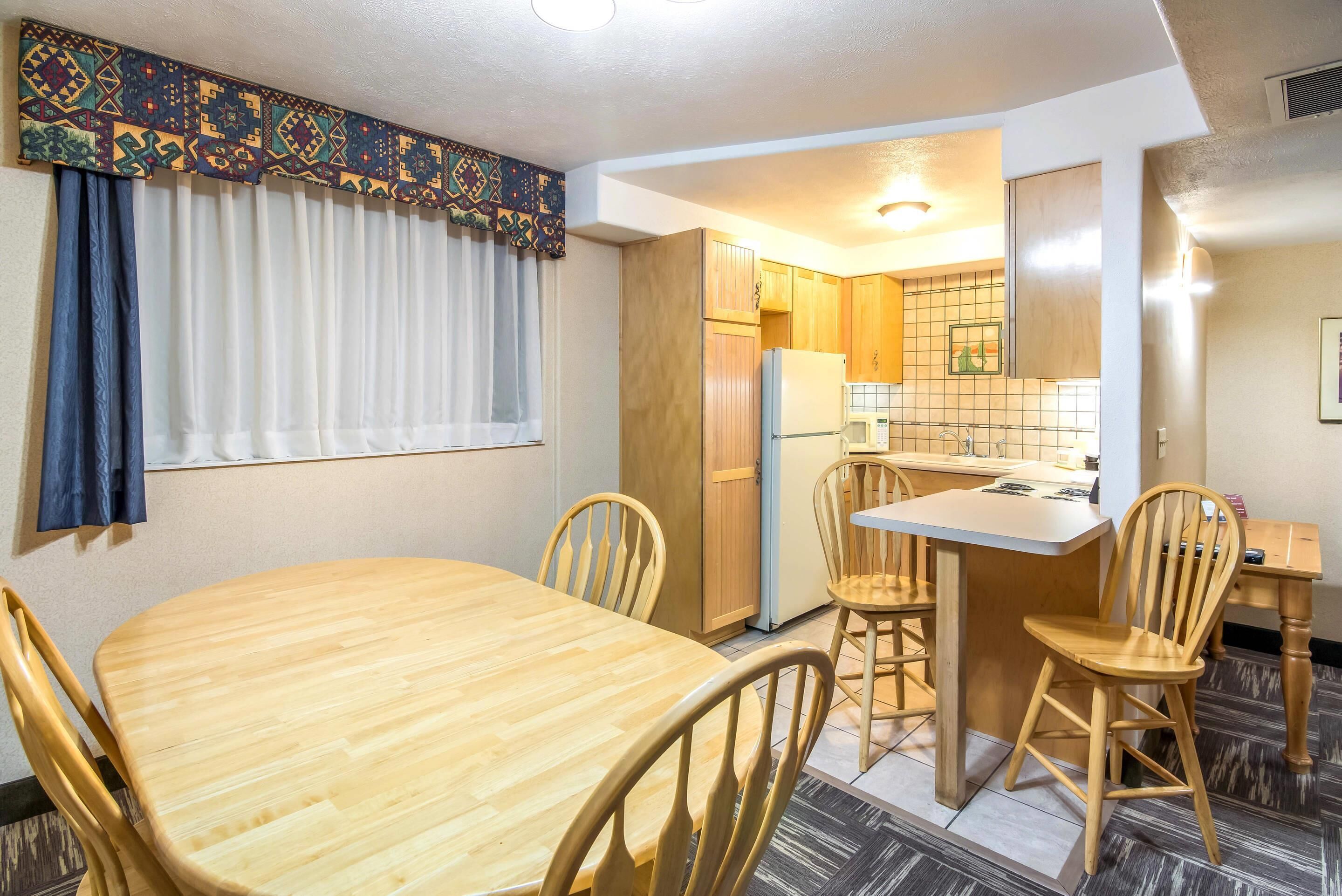Una cocina compacta con armarios de madera, un refrigerador y un comedor con una mesa y sillas.