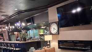 A modern lounge area with a sofa, ottoman, and bar seating, a flat-screen TV, and a clock on the wall.
