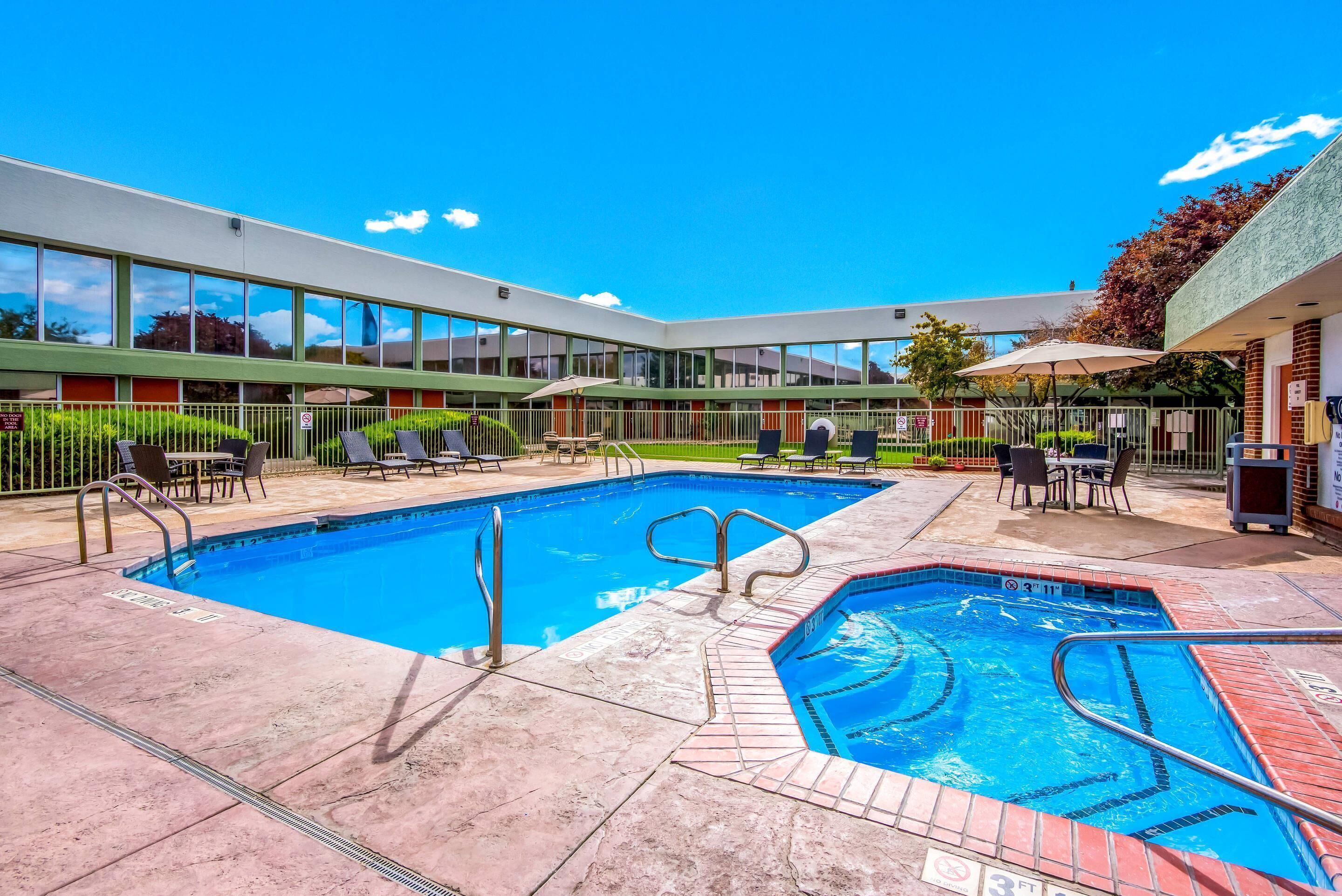 A hotel with a swimming pool, outdoor seating, and a covered patio area.