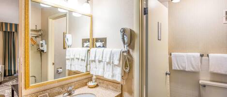 A hotel bathroom with a sink, mirror, towel rack, and toilet.