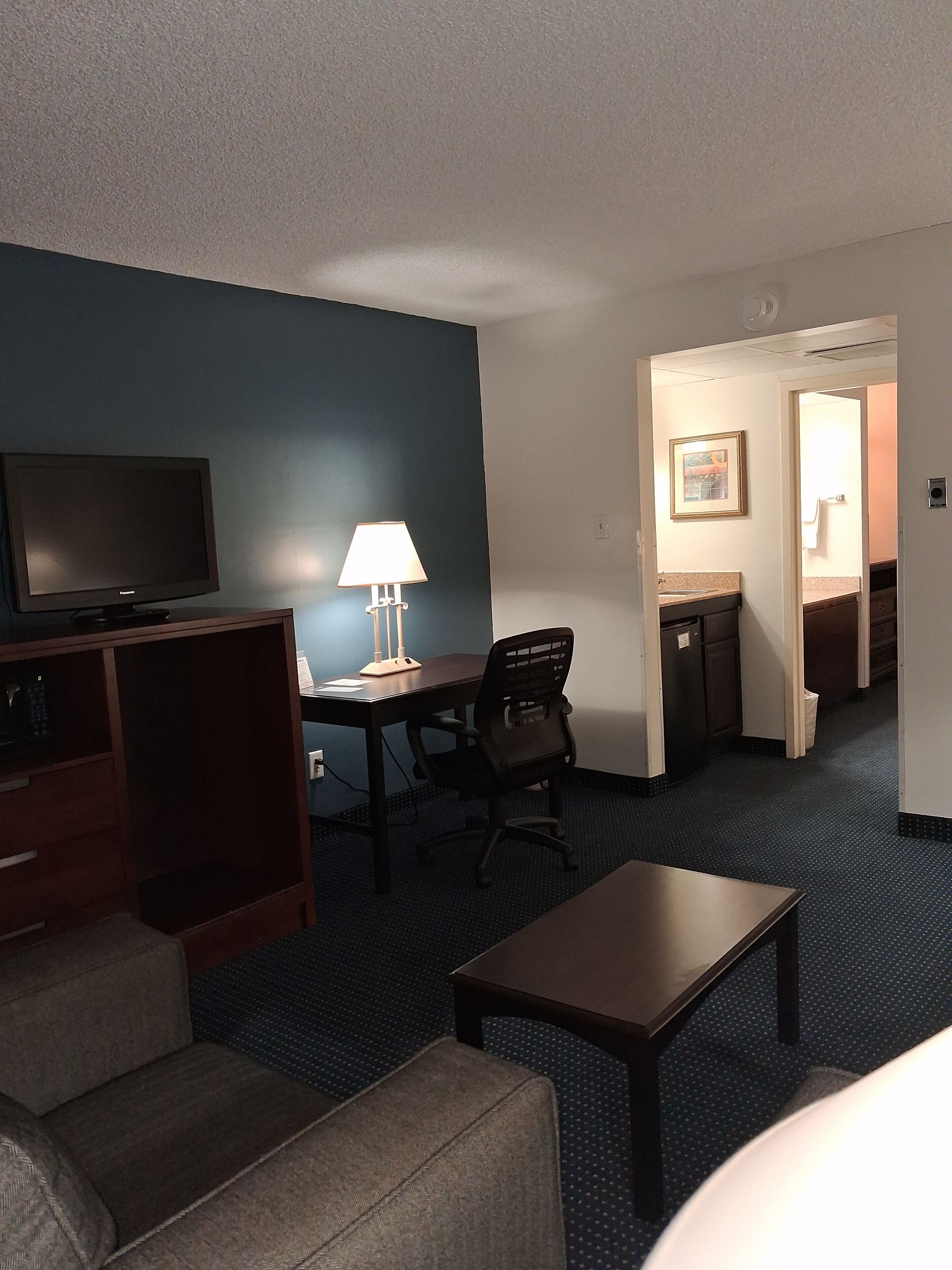Une chambre d’hôtel équipée d’une télévision, d’un bureau, d’une chaise, d’une lampe et d’une petite table.