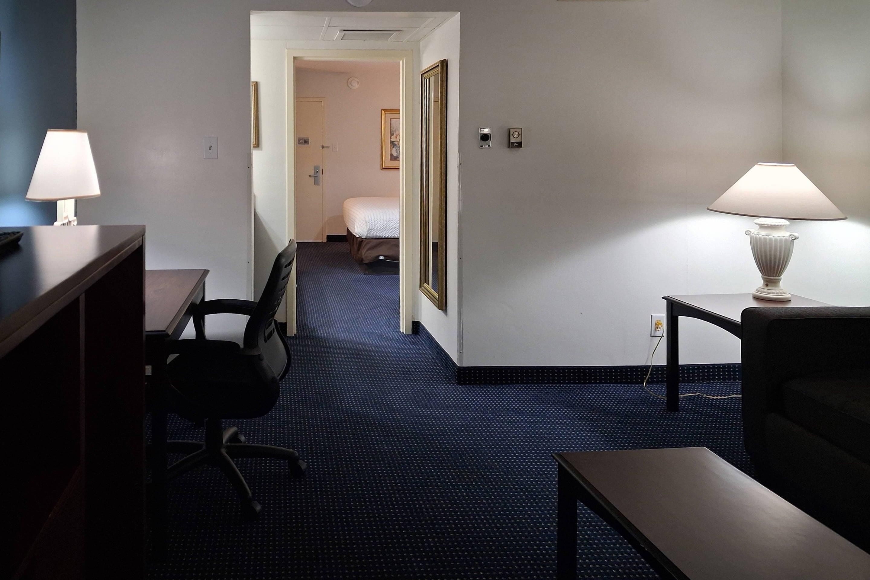 A hotel room with a desk, chair, bedside table, lamp, and a bed.
